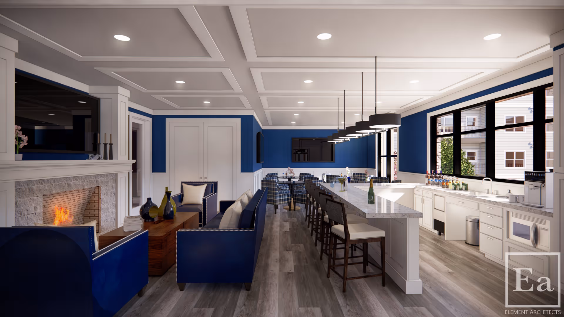 A modern and spacious common area featuring a cozy seating arrangement with blue upholstered chairs and sofas around a wooden coffee table in front of a lit fireplace. Adjacent to the seating area is a long kitchen island with bar stools, pendant lighting, and a countertop with various bottles and a coffee machine. Large windows let in natural light, and the walls are decorated with blue and white paneling.