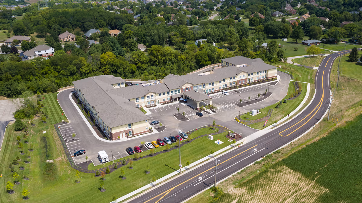 Aerial view of a large two-story assisted living facility with parking, landscaped grounds, and a curved road.
