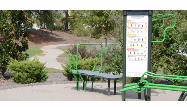 Outdoor exercise equipment with green frames and instructional sign in a landscaped area.