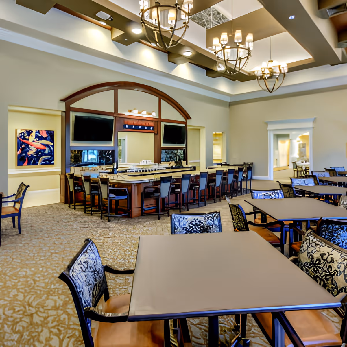 Spacious dining and lounge area with multiple tables and chairs and a central bar under decorative chandeliers.