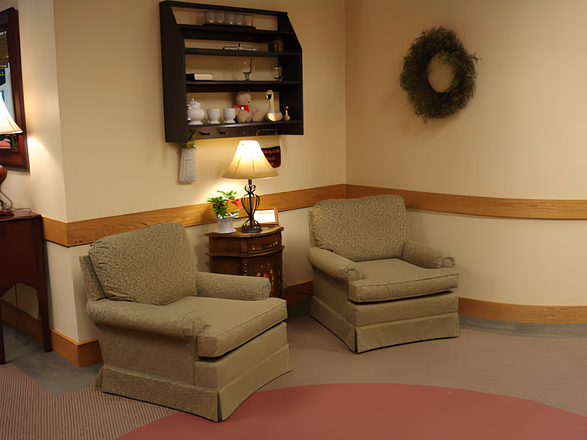 Two upholstered armchairs flanking a small side table with a lamp in a cozy corner of a communal lounge.