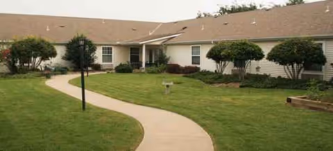 Single-story senior housing building with a winding sidewalk and a well-kept lawn.