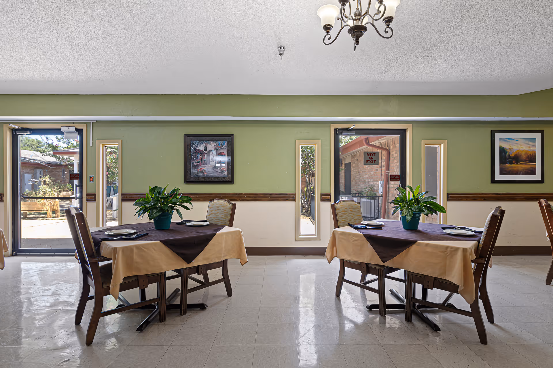 Dining room with two set tables, potted plants, chairs, and doors leading to an outdoor area.