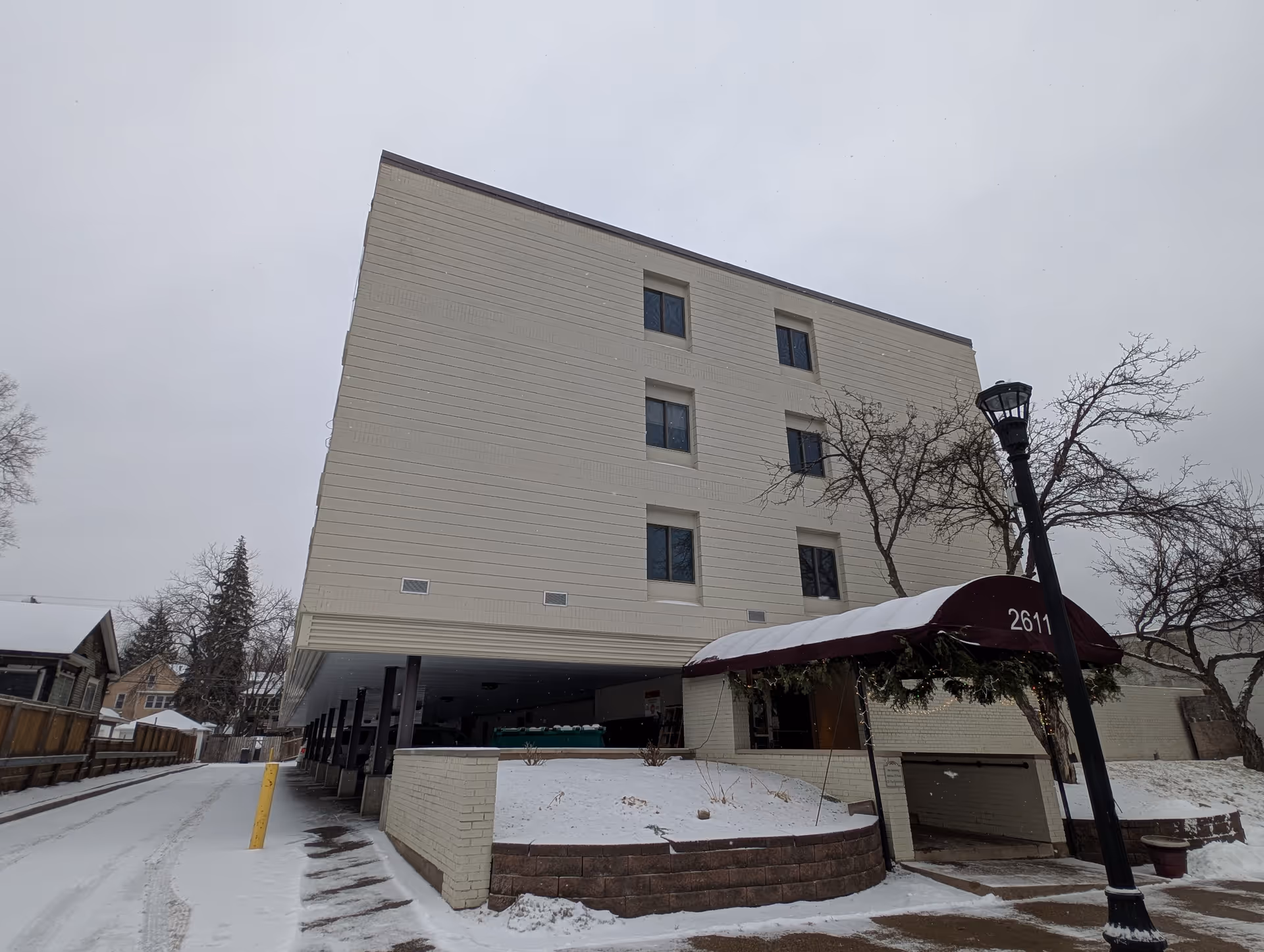 Four-story light-colored building with a maroon covered entrance canopy marked "2611" and snow on the ground.
