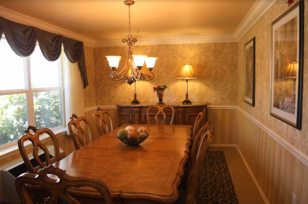 Formal dining room with a long wooden table and chairs, a chandelier, sideboard with a lamp, and a window with drapes.
