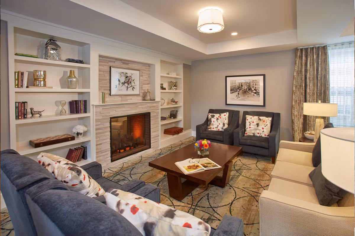 Cozy furnished living room with sofas, armchairs, a coffee table, built-in shelves, and a fireplace.