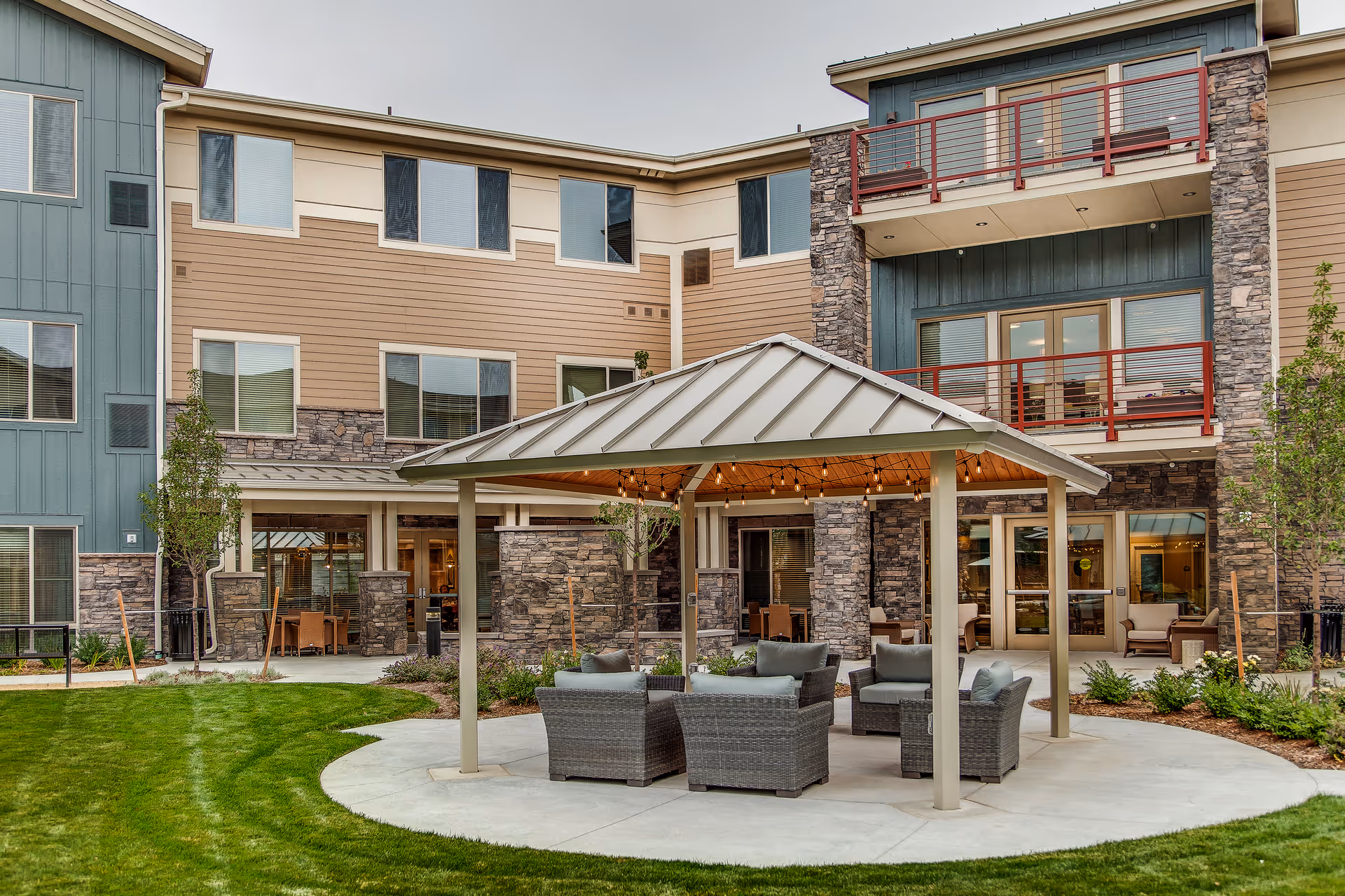 Outdoor courtyard of a multi-story senior living building with a covered pavilion and wicker seating.