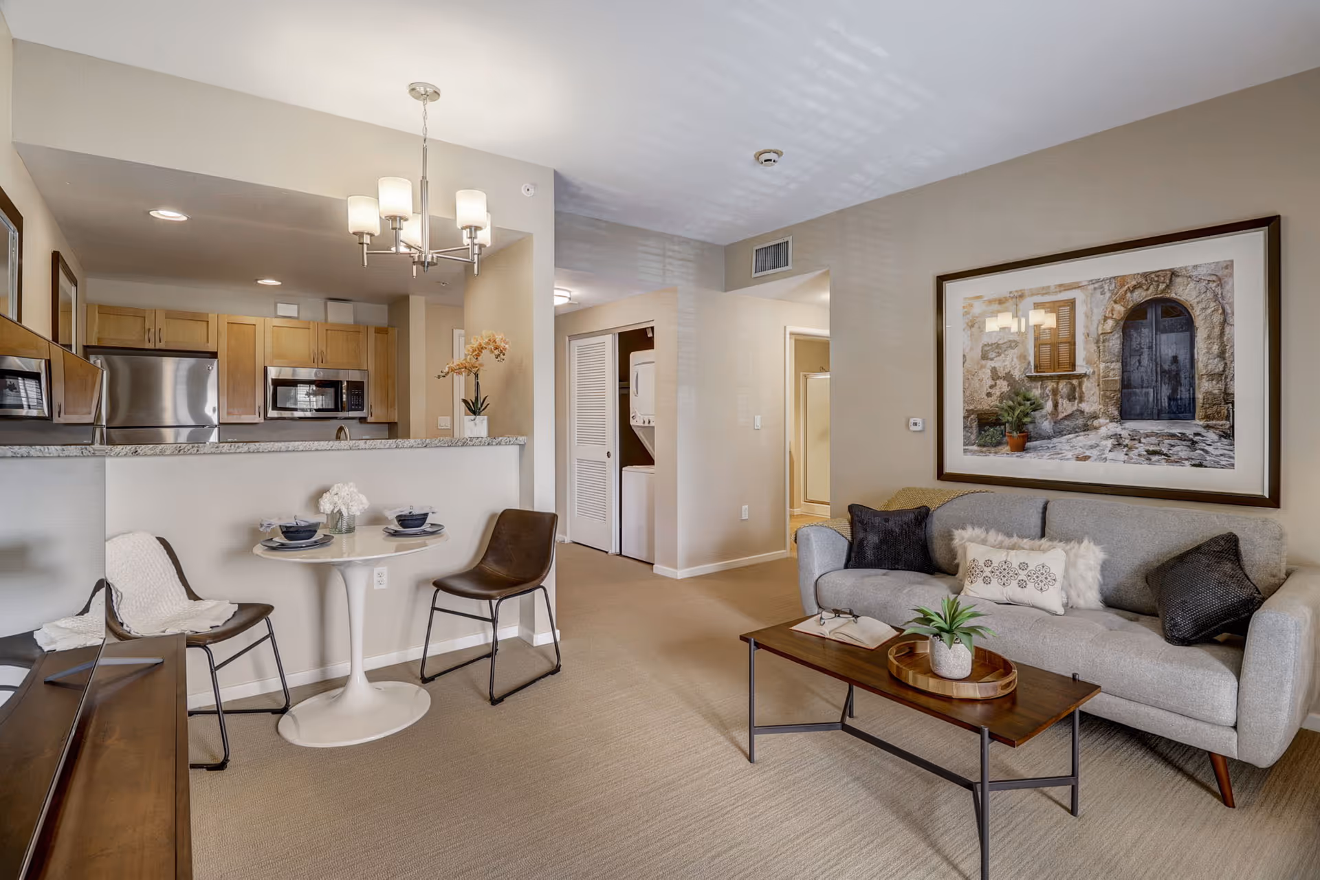 Open-plan living room and kitchen with a sofa, coffee table, small dining table, and stainless steel appliances.