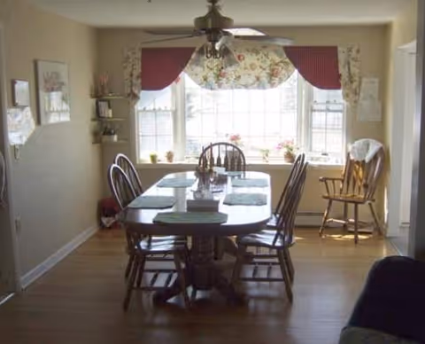 Dining room in a senior living facility with a wooden table, chairs, and a large window.