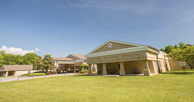 Exterior view of a single-story building with a covered entrance and a well-maintained lawn under a clear blue sky.