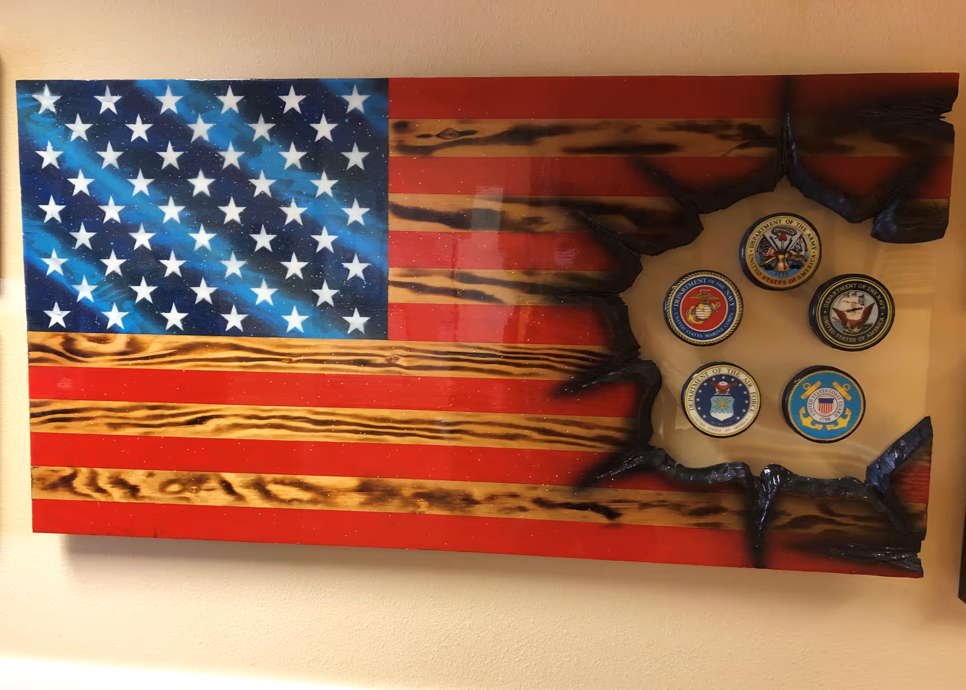 A wooden American flag wall art with a burnt effect on the right side, revealing five circular emblems representing different branches of the United States military: Army, Marine Corps, Navy, Air Force, and Coast Guard.