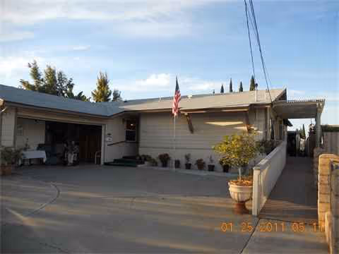 Single-story facility exterior with driveway, carport, flag, and potted plants along walkway.