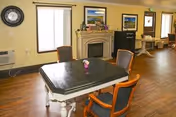 A communal room featuring a rectangular dining table with chairs, a small vase, a fireplace mantel, a television, and windows.