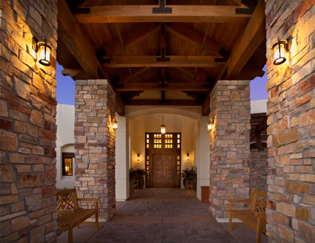 Covered stone-pillared entrance with wooden beams, lanterns, benches, and a carved wooden front door.
