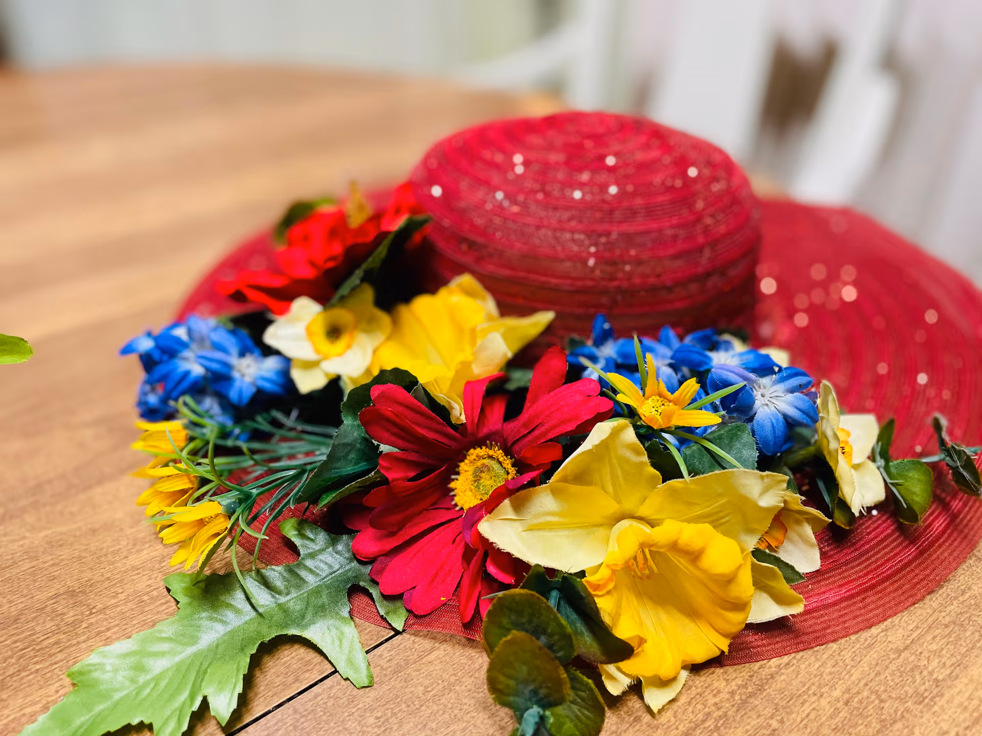 Red wide-brimmed hat decorated with colorful artificial flowers resting on a wooden table.
