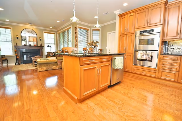 Bright open kitchen with a central island and hardwood floors opening into a living room with a fireplace.