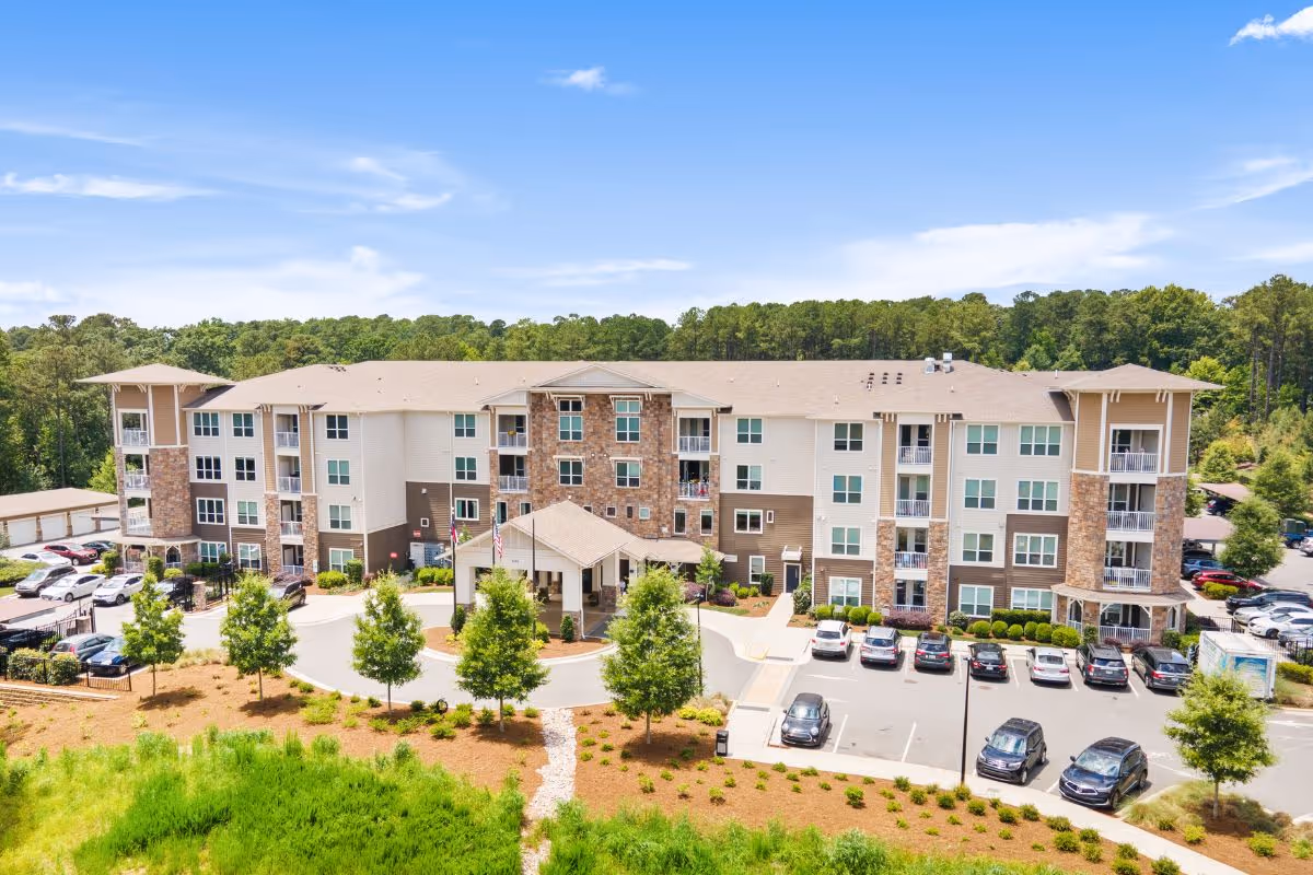 A multi-story senior living building with balconies, parking, and surrounding trees.