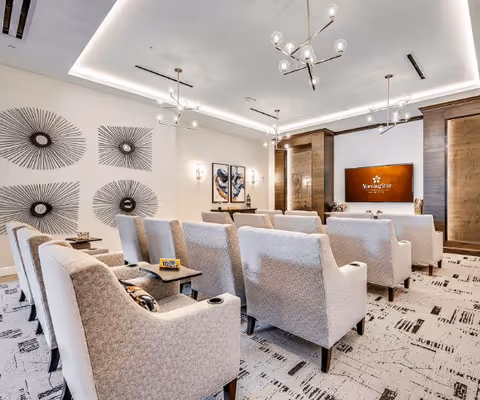A modern, well-lit common area with rows of comfortable beige armchairs facing a wooden wall with a mounted screen displaying the MorningStar logo. The room features decorative wall art, contemporary light fixtures, and a patterned carpet.