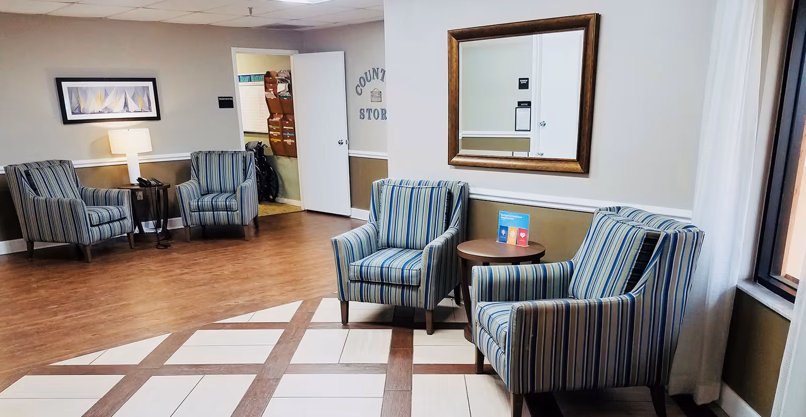 Interior seating area with striped armchairs, side tables, a mirror on the wall, and an open doorway to a storage room.