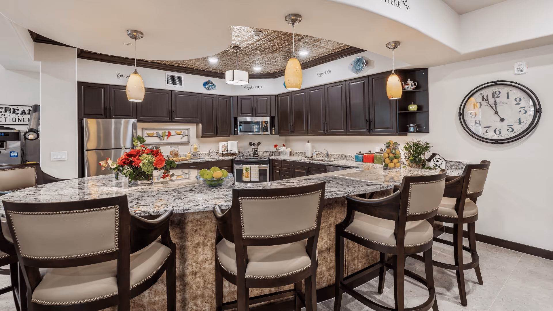 Spacious modern kitchen with a large marble island and bar seating, dark cabinets, pendant lights, and stainless steel appliances.