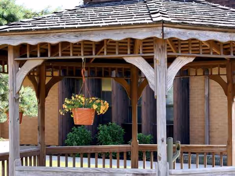 Wooden gazebo with hanging plant pot and greenery in outdoor facility area