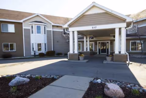 Exterior view of a senior living facility entrance with covered walkway and landscaping.