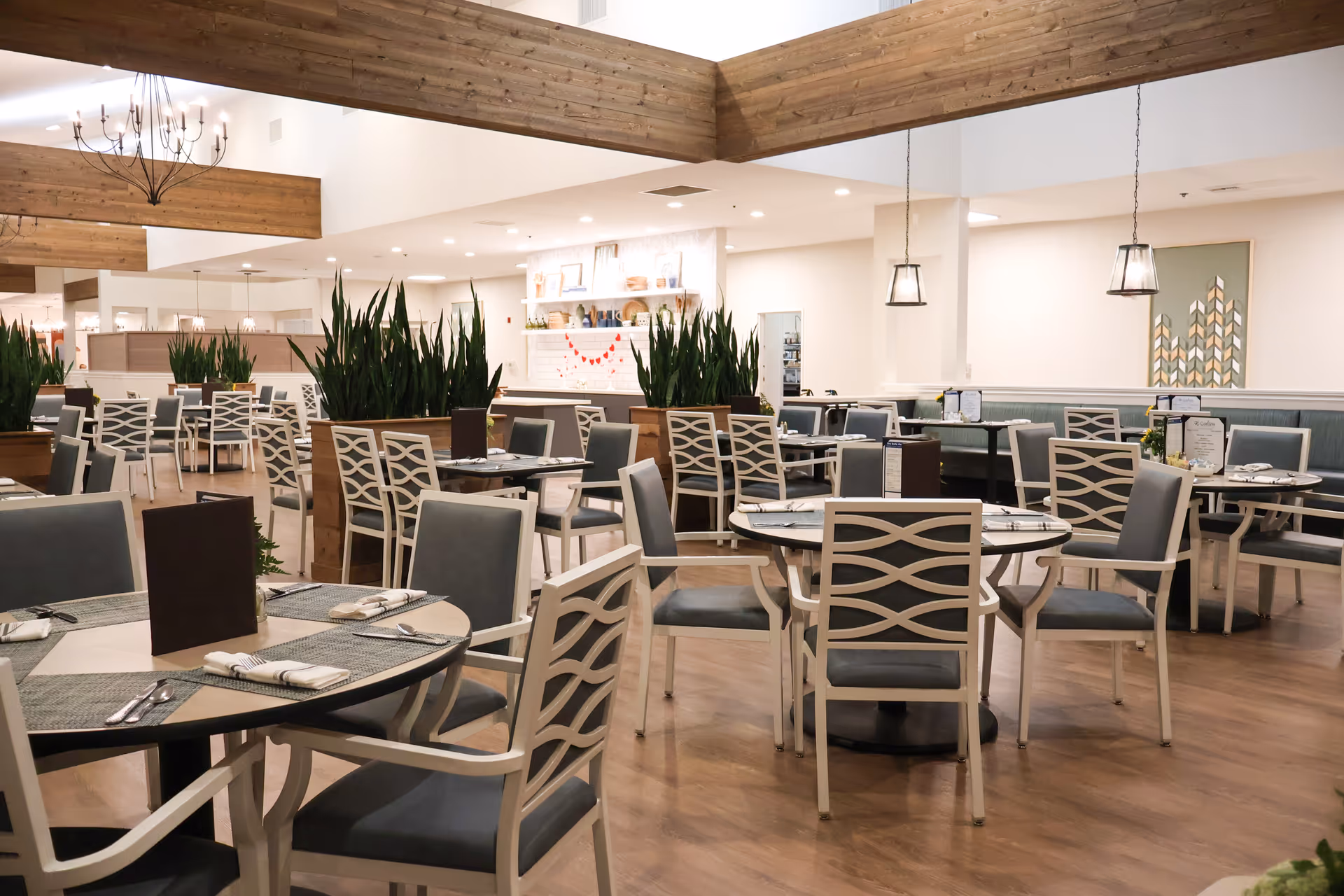 Spacious dining room with round tables, patterned chairs, potted plants and pendant lighting.