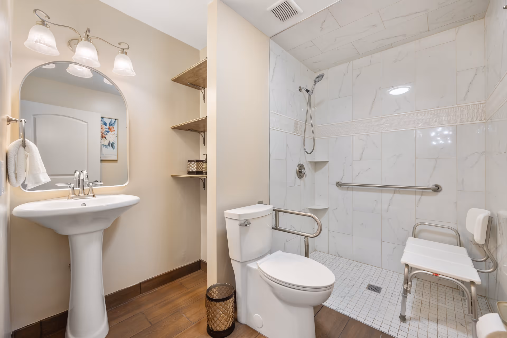 Accessible bathroom with a pedestal sink, toilet and roll-in tiled shower with grab bars and a shower chair.