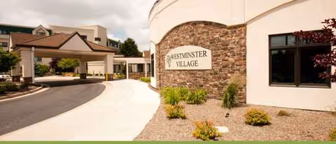 Curved brick exterior of Westminster Village with driveway and landscaped entrance.