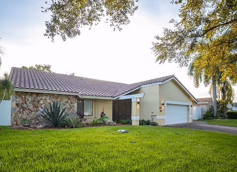 Exterior view of a single-story care facility with beige walls, stone accents, and a garage.