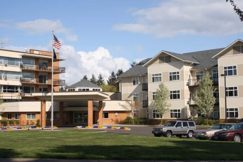 Exterior view of Friendsview Retirement Community with lawn, flagpole, and parked cars.