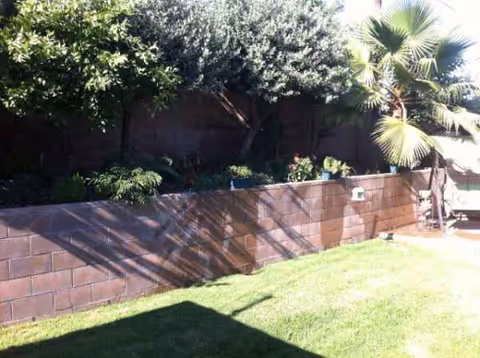 Outdoor area with a brick planter wall, trees, and a green lawn.
