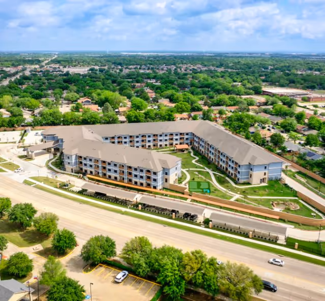 Aerial view of a U-shaped senior living building surrounding a landscaped courtyard in a suburban neighborhood.