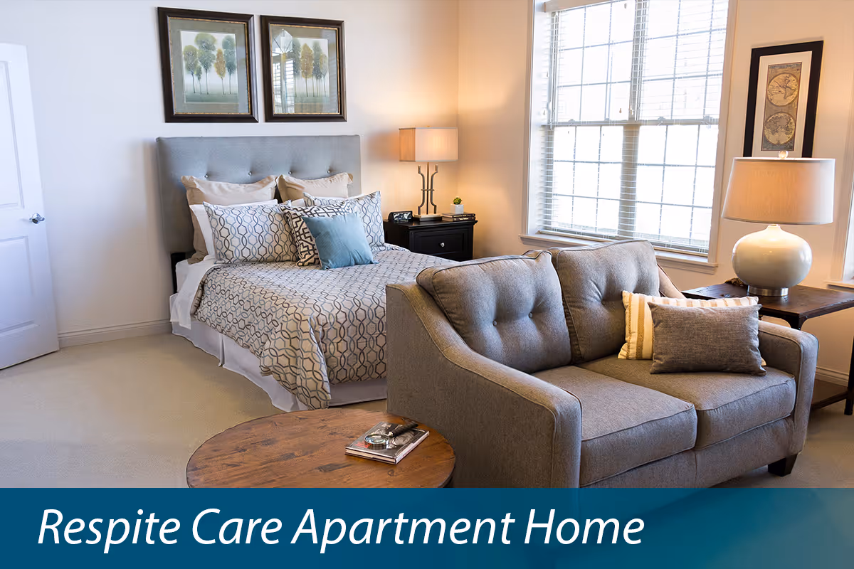 A furnished studio-style apartment interior with a bed, loveseat, lamps, and a coffee table by a window.