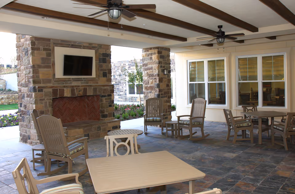 Covered outdoor patio with a stone fireplace and mounted TV, ceiling fans, and several tables and chairs.