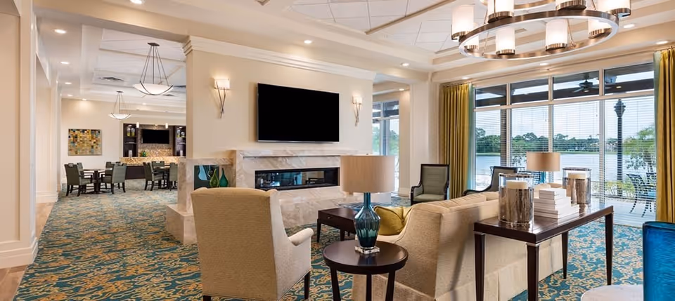 Bright communal lounge with sofas, armchairs, a fireplace and large windows overlooking a lake.