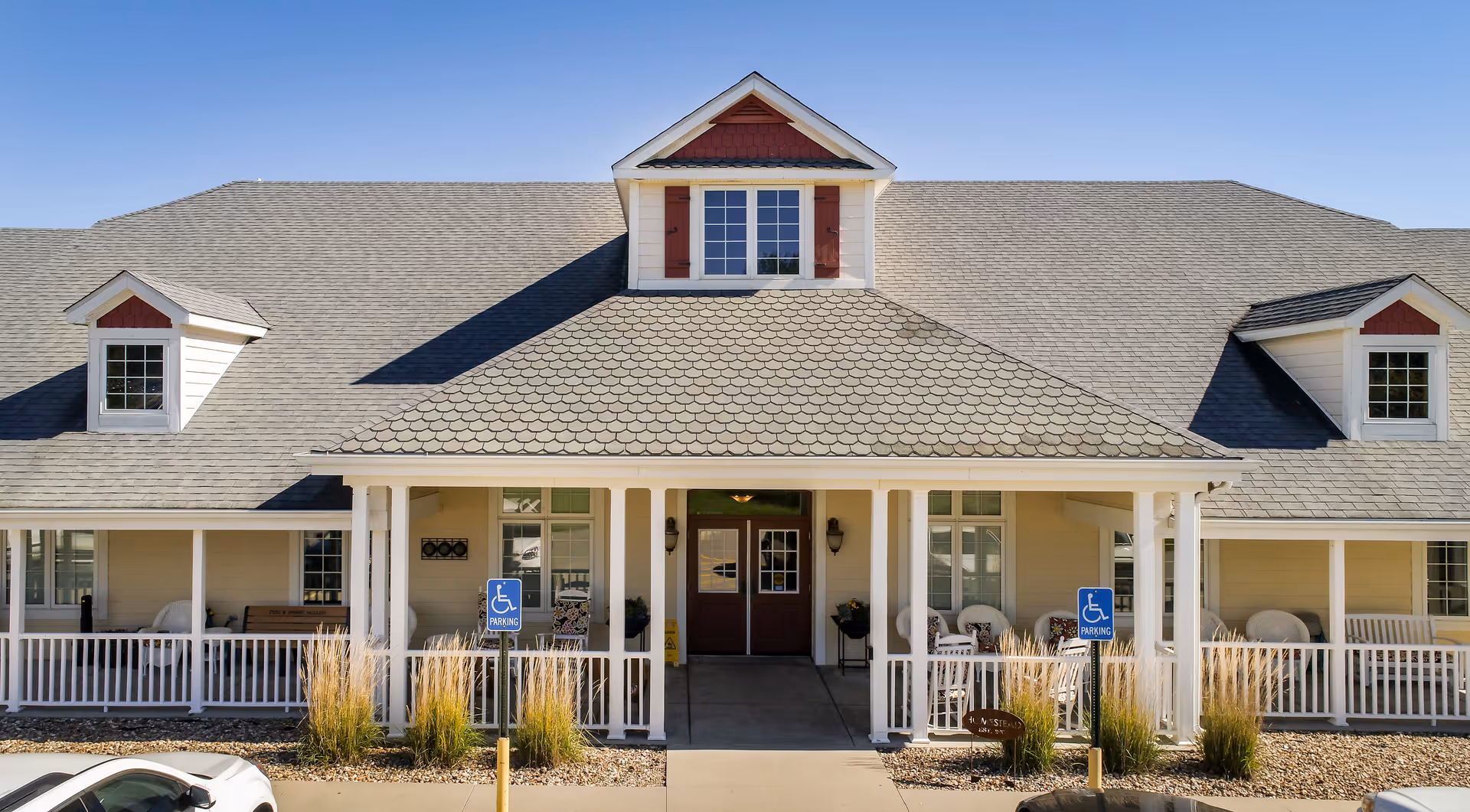 Front exterior of a single-story assisted living building with a covered porch, white railing, and accessible parking signs.