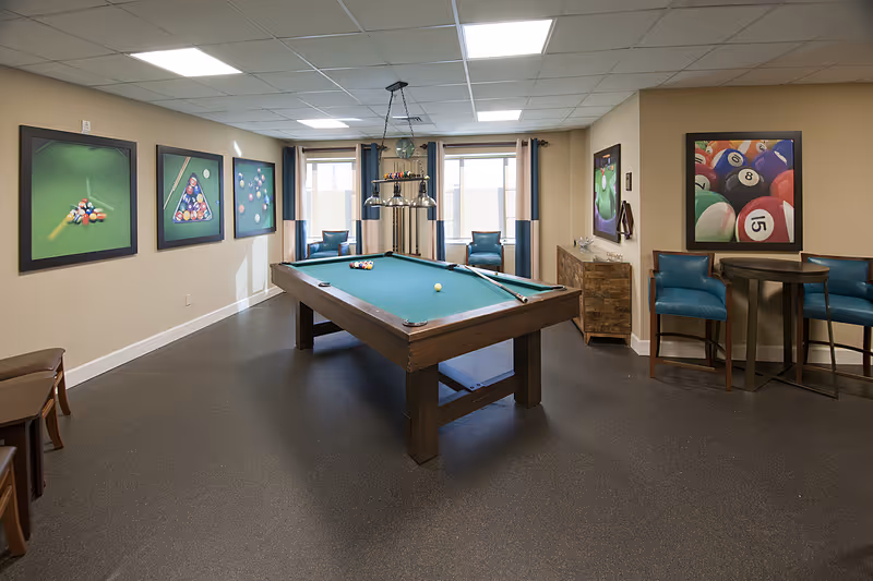Interior recreation room featuring a pool table in the center, seating, framed billiards artwork, and overhead lights.