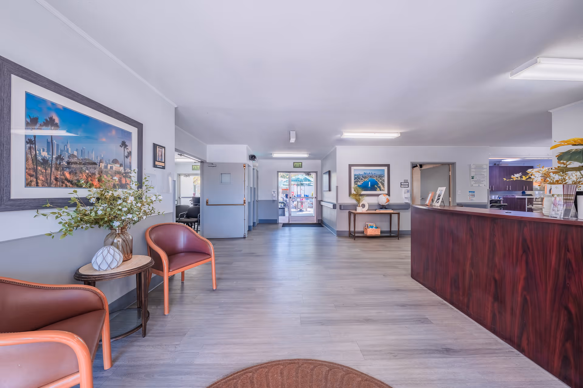 Bright reception lobby with seating, potted plants, framed artwork, and a long wooden front desk.