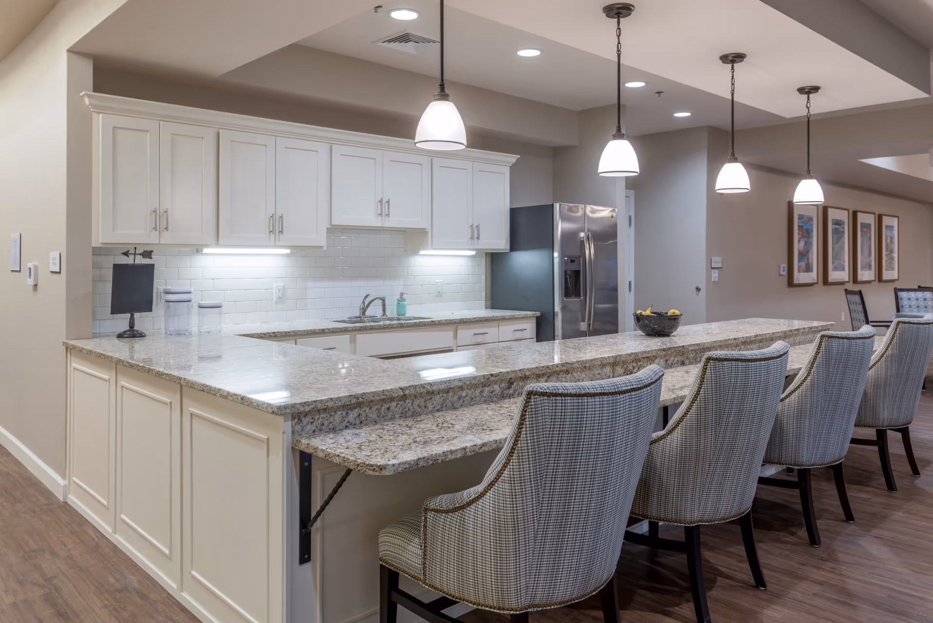 Bright open kitchen with a long granite island, upholstered bar stools and pendant lights.