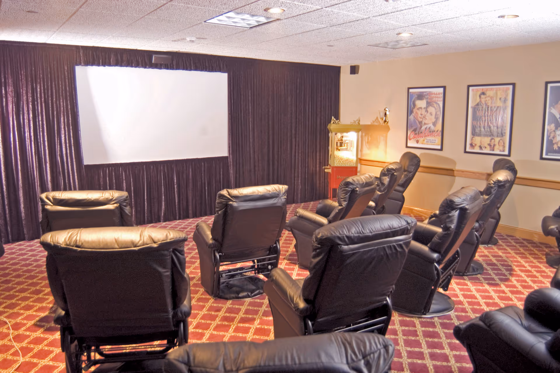 A small theater room with leather recliner seats facing a projection screen and a popcorn machine.