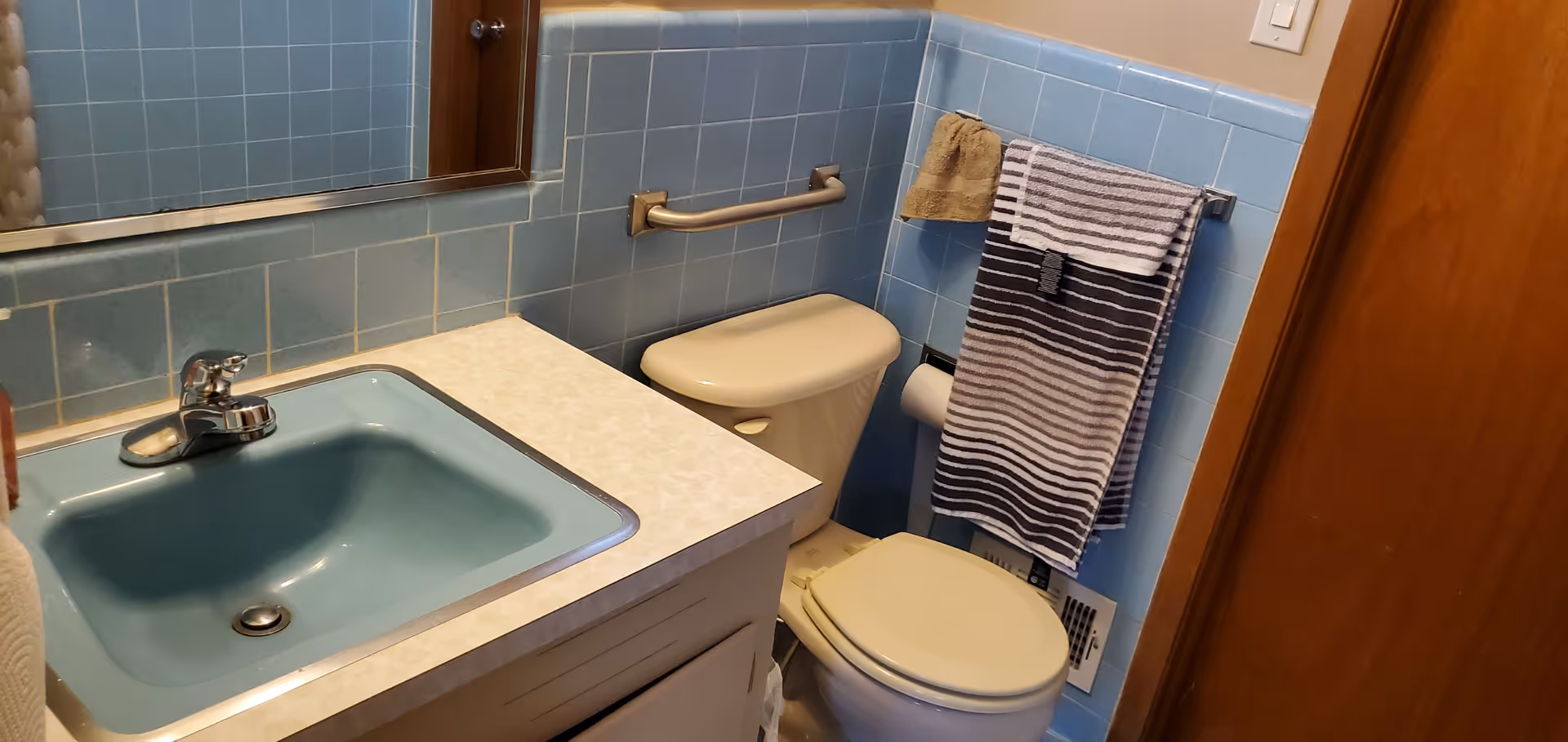 Small bathroom with a blue sink and tiled walls, a toilet, mirror, and a striped towel on a rack.