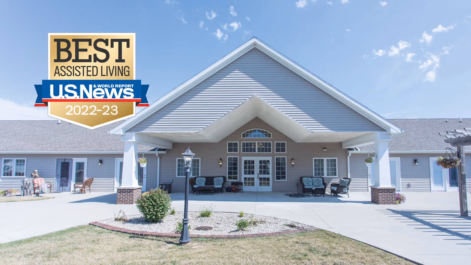 Front entrance of a single-story assisted living building with a covered portico, outdoor seating, and landscaping.