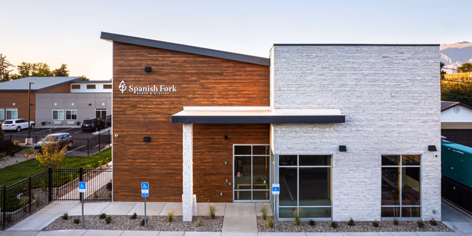 Front exterior of Spanish Fork Rehab & Nursing showing a modern wood and white stone facade with the main entrance and accessible parking.