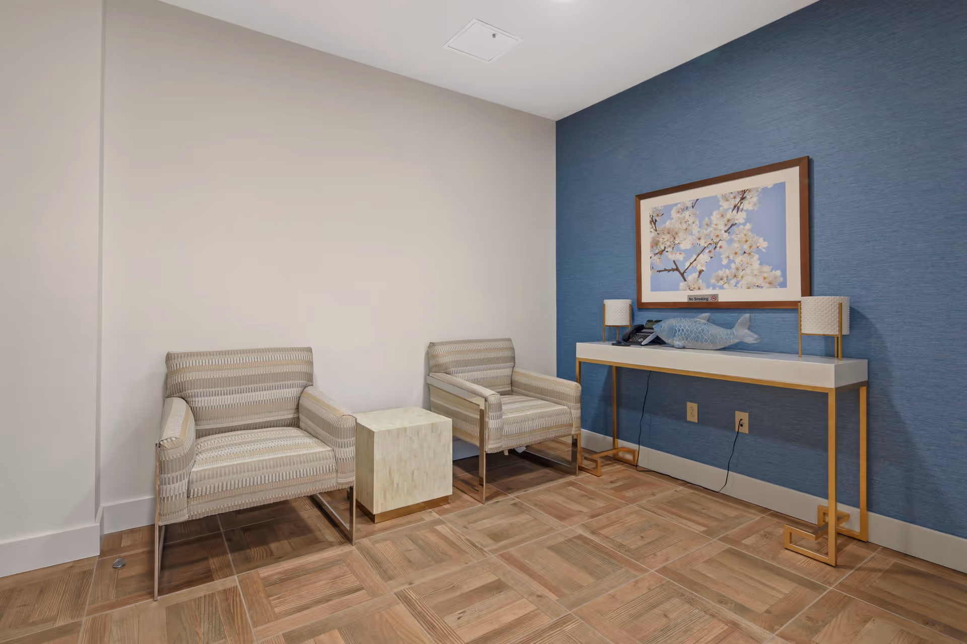 Small sitting area with two striped armchairs, a cube side table, and a console table beneath framed artwork on a blue accent wall.