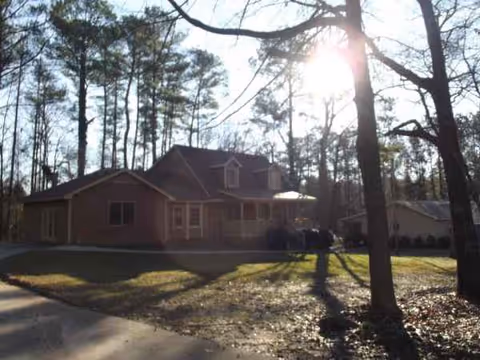 Exterior view of a brick senior living building surrounded by trees and sunlight.