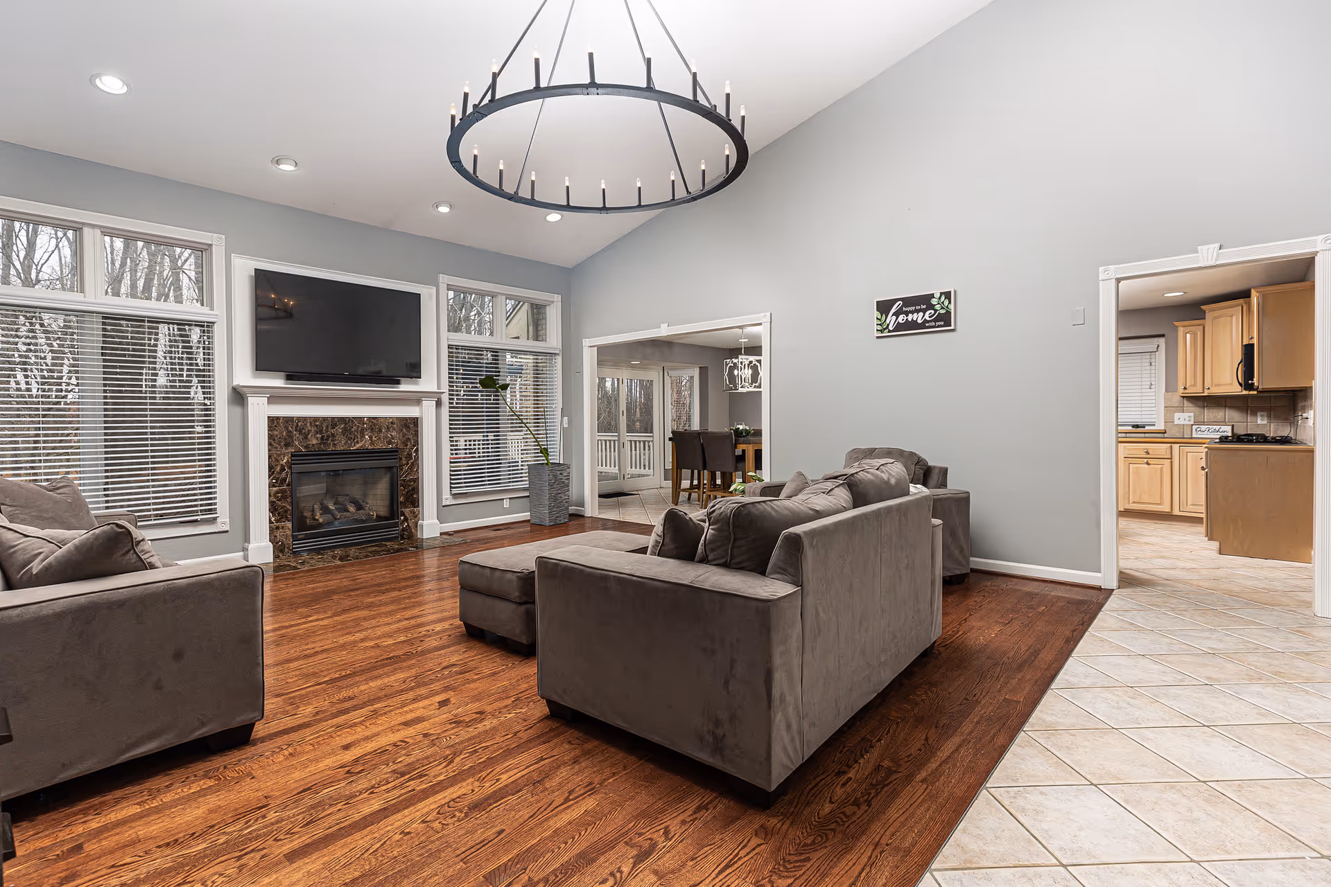Spacious living room with gray sofas, a fireplace under a wall-mounted TV, hardwood floors and large windows.