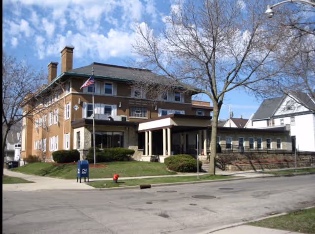 Exterior view of a two-story brick senior living facility with a covered entrance and flag.