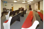 Small chapel-style meeting room with wooden pews fitted with red cushions, a podium, and a piano at the front.