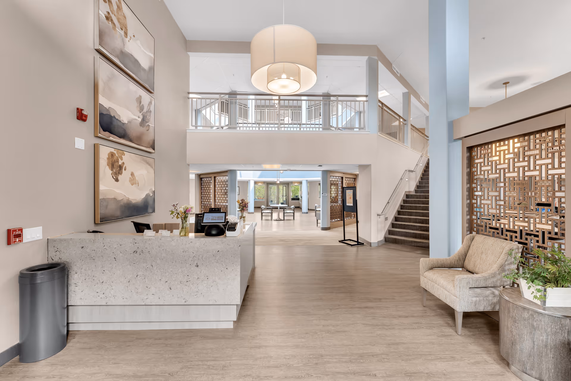 Spacious modern senior living lobby with a reception desk, seating area, staircase to an upper level, and decorative partitions.